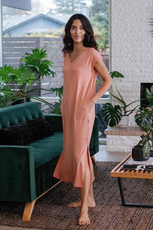 A woman standing with both hands in her pockets, wearing Yala Sloane V-Neck Cap Sleeve Bamboo Maxi Dress in Apricot
