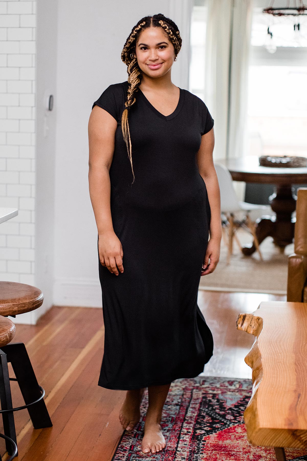 A woman standing and smiling with one foot forward, wearing Yala Sloane V-Neck Cap Sleeve Bamboo Maxi Dress in Black