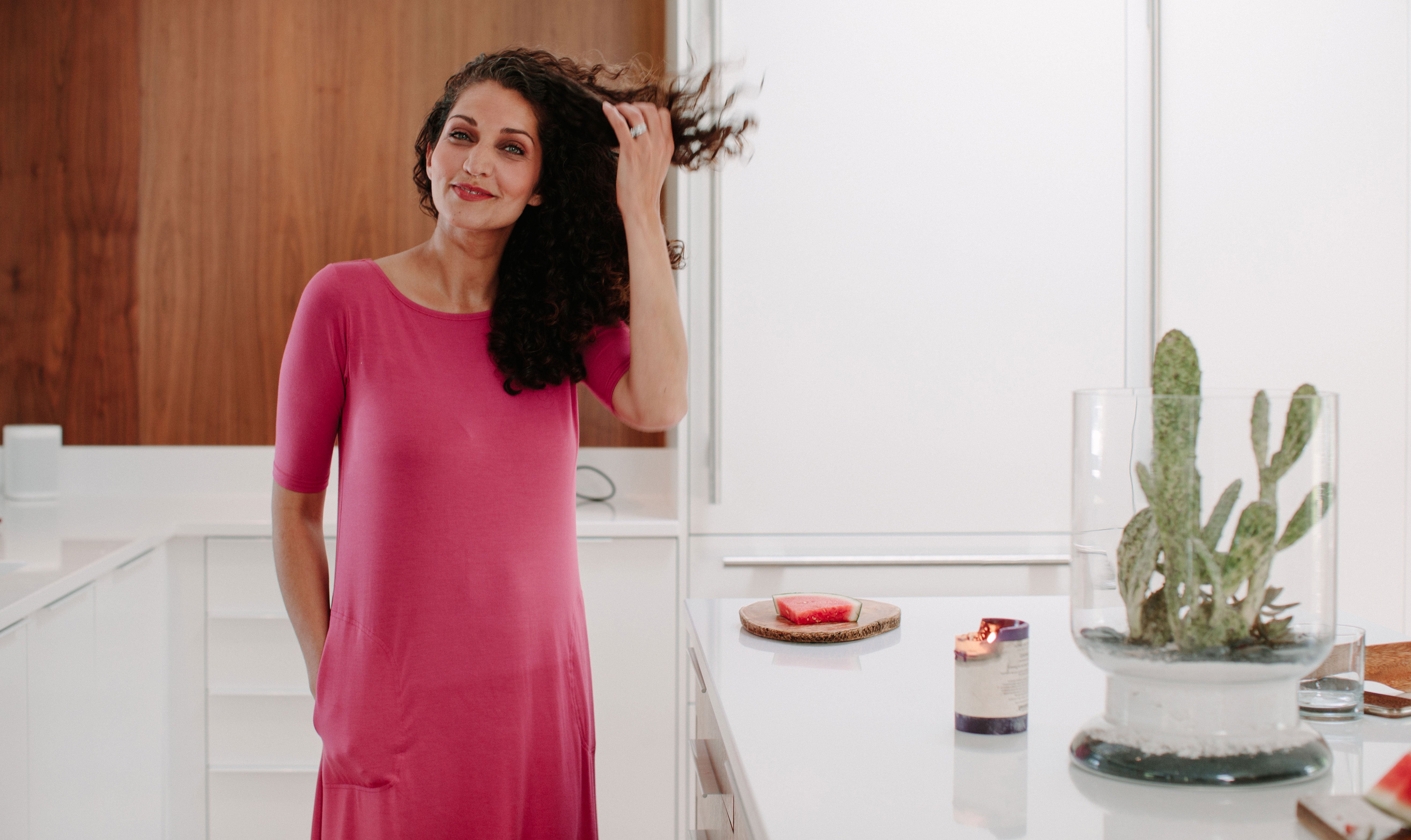 Woman standing in a kitchen wearing a pink YALA Maraya Dress, hands in pockets.