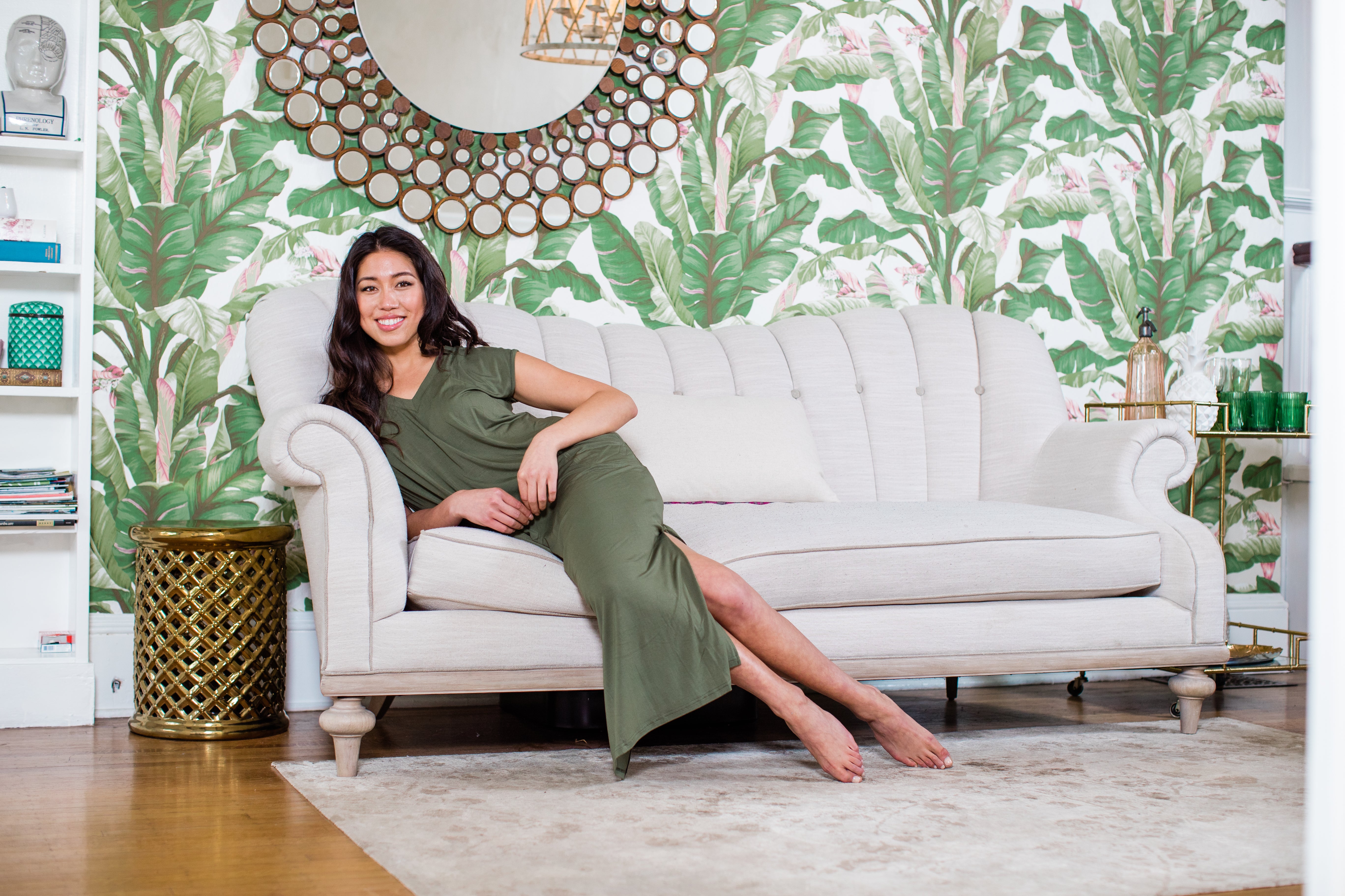 Woman lounging in a green YALA Sloan Dress in a tropical vacation home