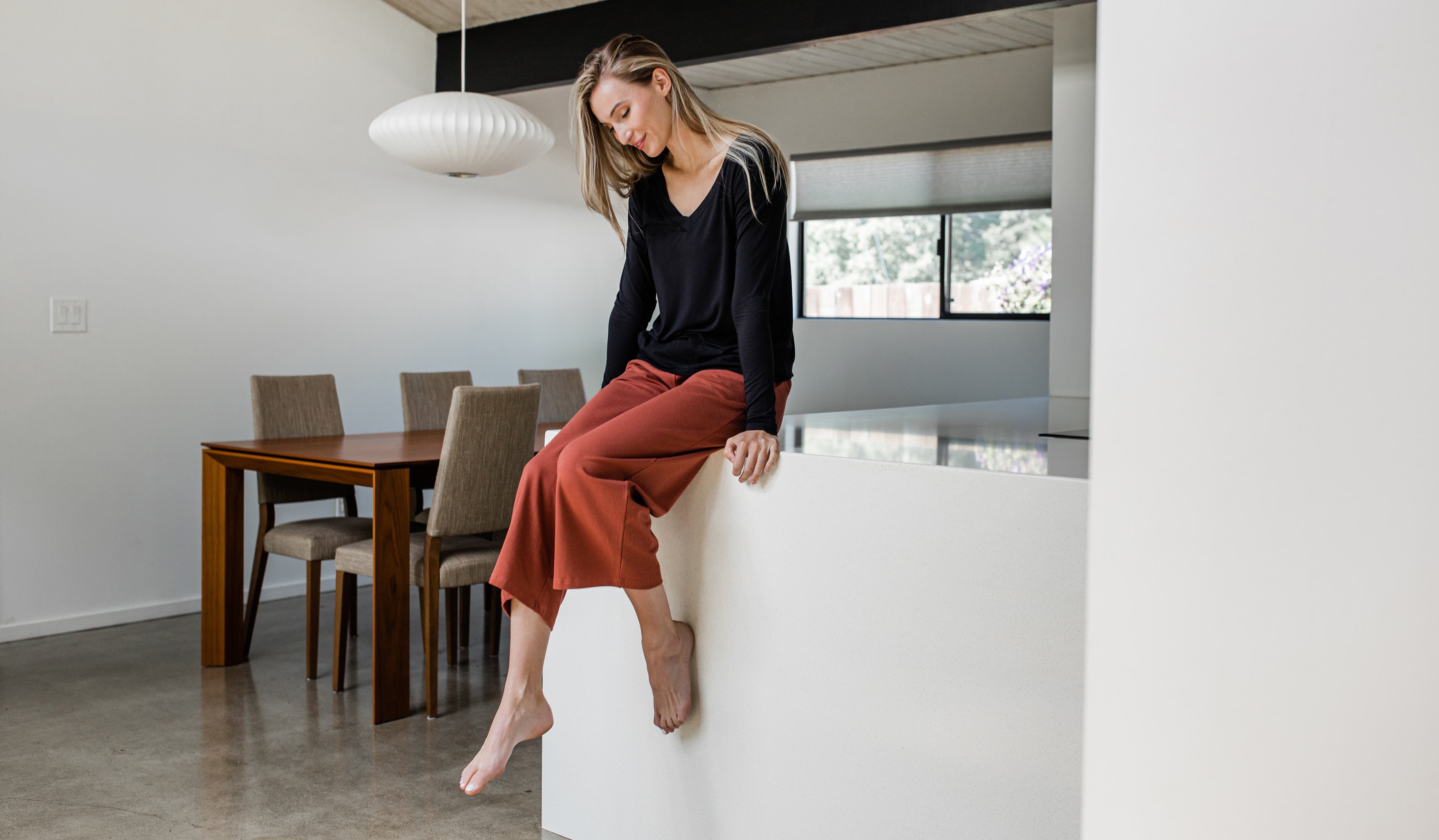 A woman sitting on a kitchen counter wearing YALA's Cropped Billie Pant.