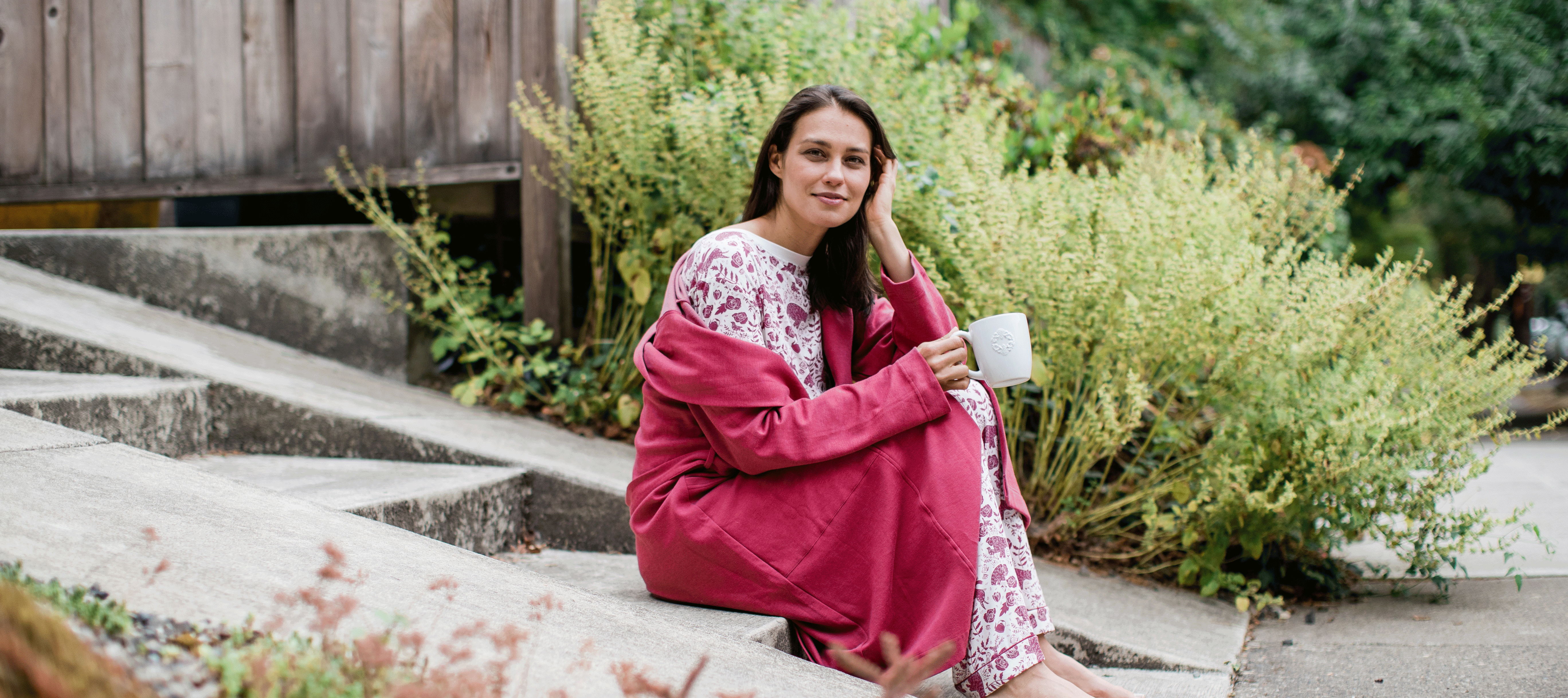 Woman drinking coffee on a porch in a hooded YALA Elliot robe.