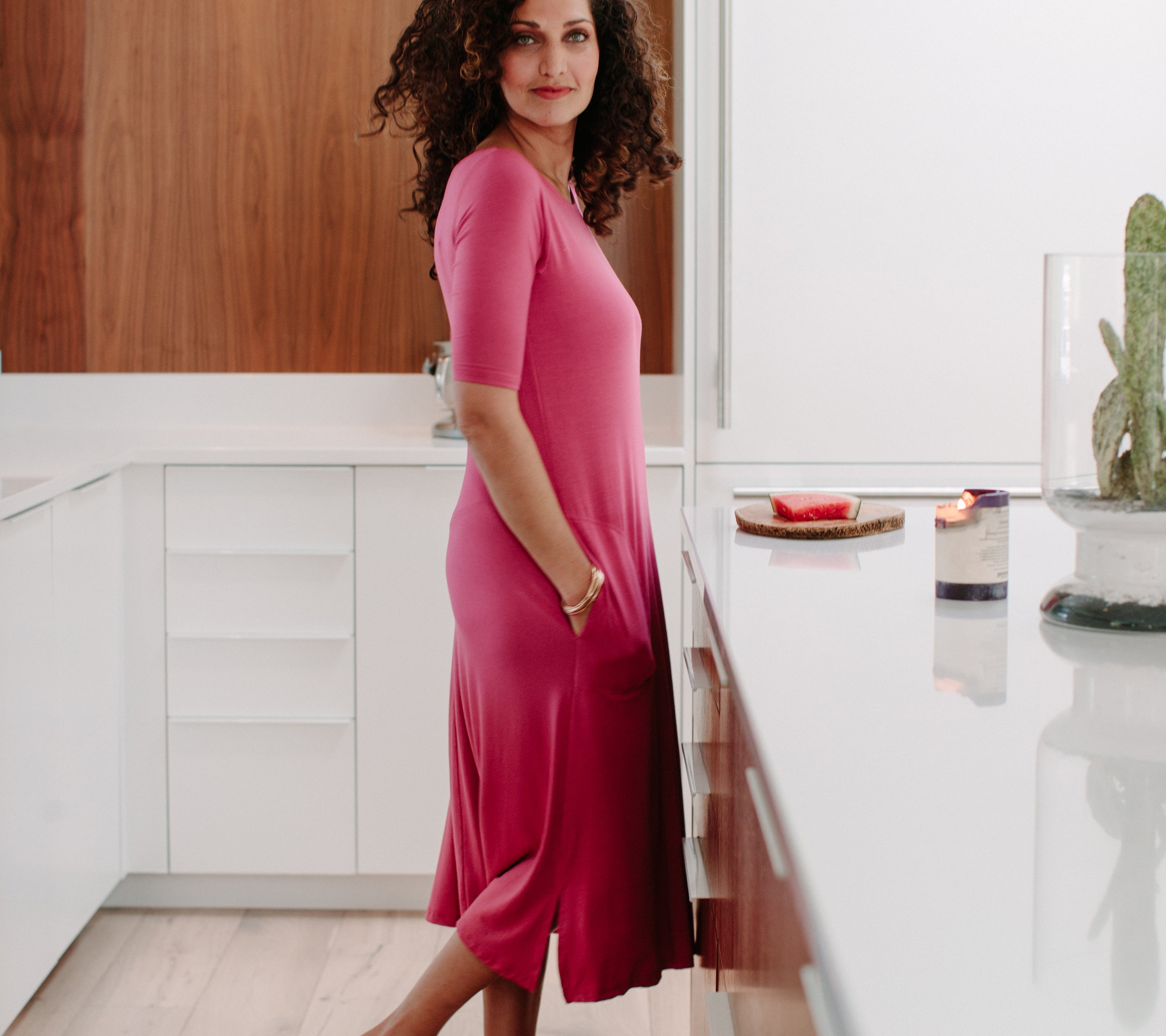 Woman standing in a kitchen wearing a pink YALA Maraya Dress, hands in pockets.
