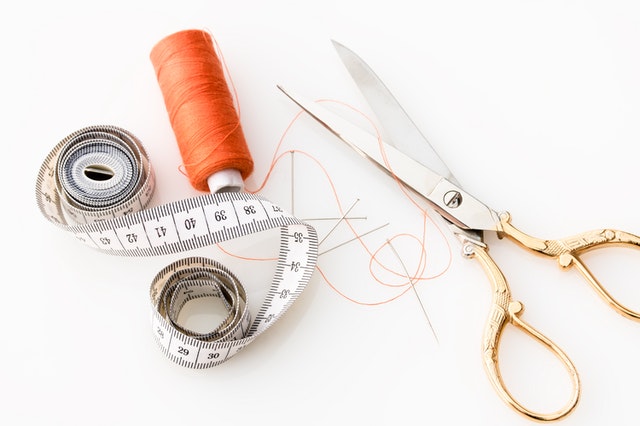 Sewing tools on a table. Scissors, thread, and a measuring tape. 