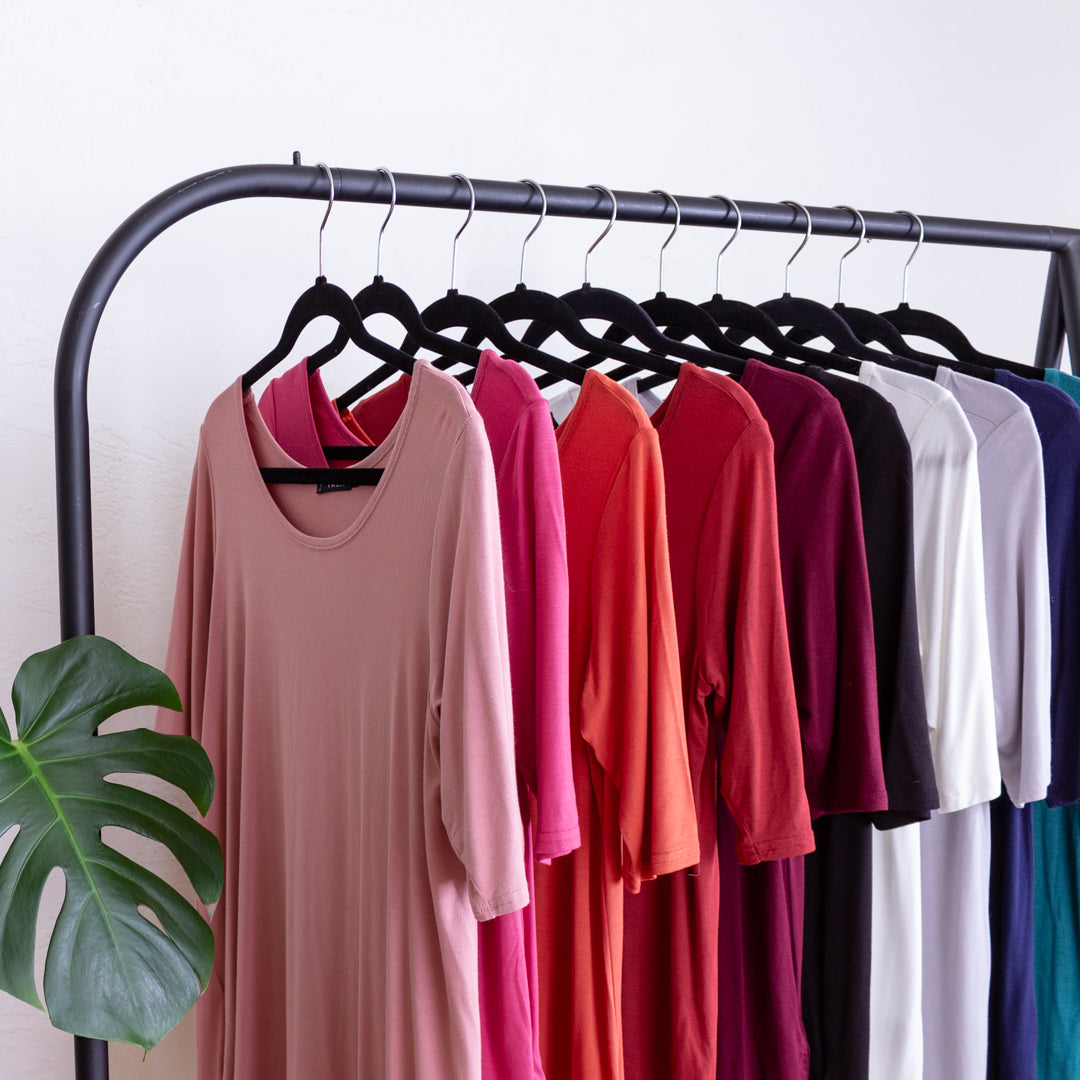 A rainbow assortment of shirts hanging on a clothing rack.