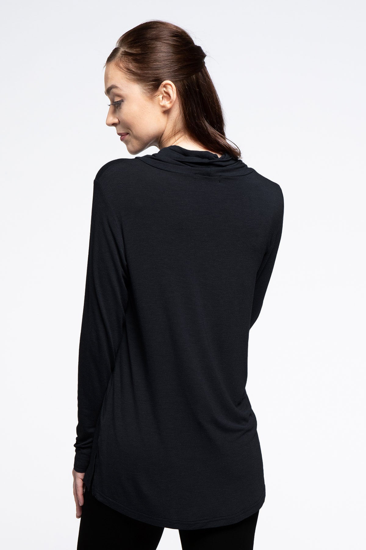 A woman standing with her back to the camera, her head turned to the side, wearing Yala Harper Cowl Neck Long Sleeve Bamboo Shirt in Black