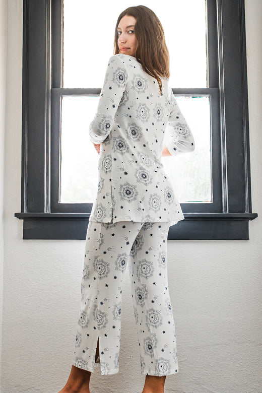 A woman standing facing a window with her back to the camera while looking back over her shoulder, waering Yala Haley Crossover Front 3/4 Sleeve Bamboo Pajama Set in Celestial Print