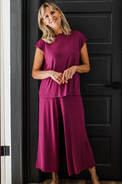 A woman standing in a doorway and smiling with her hands held in front of her, wearing Yala Opal Swing Lounge Bamboo Pajama Set in Boysenberry