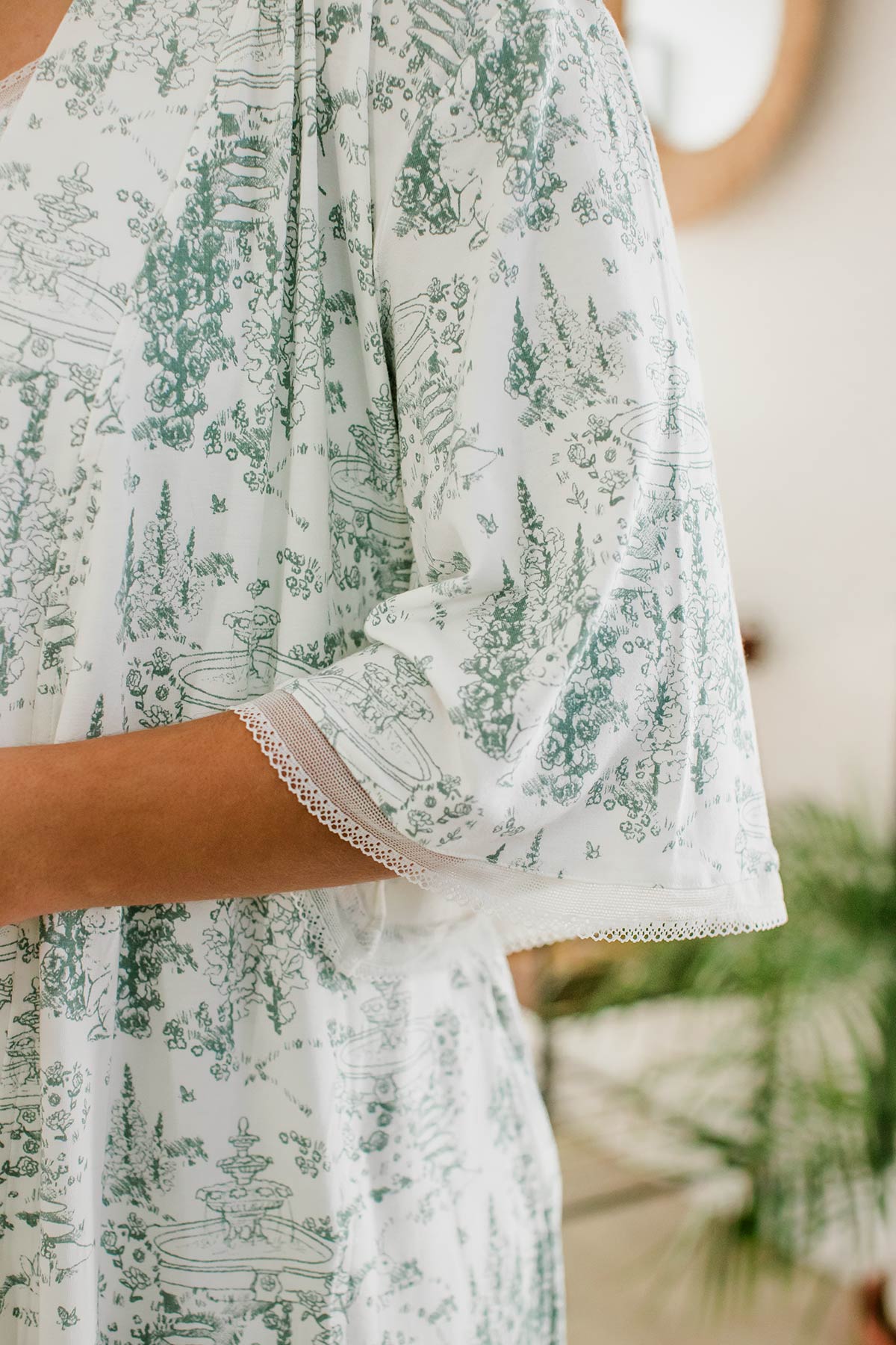 A close shot of a woman's elbow, showcasing the lace hem, wearing Iris Kimono Sleeve Belted Bamboo Lace Robe in English Garden Print