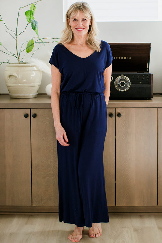 A woman standing and smiling with one hand in her pocket, wearing yala Kiova V-Neck Bamboo Jumpsuit in Navy