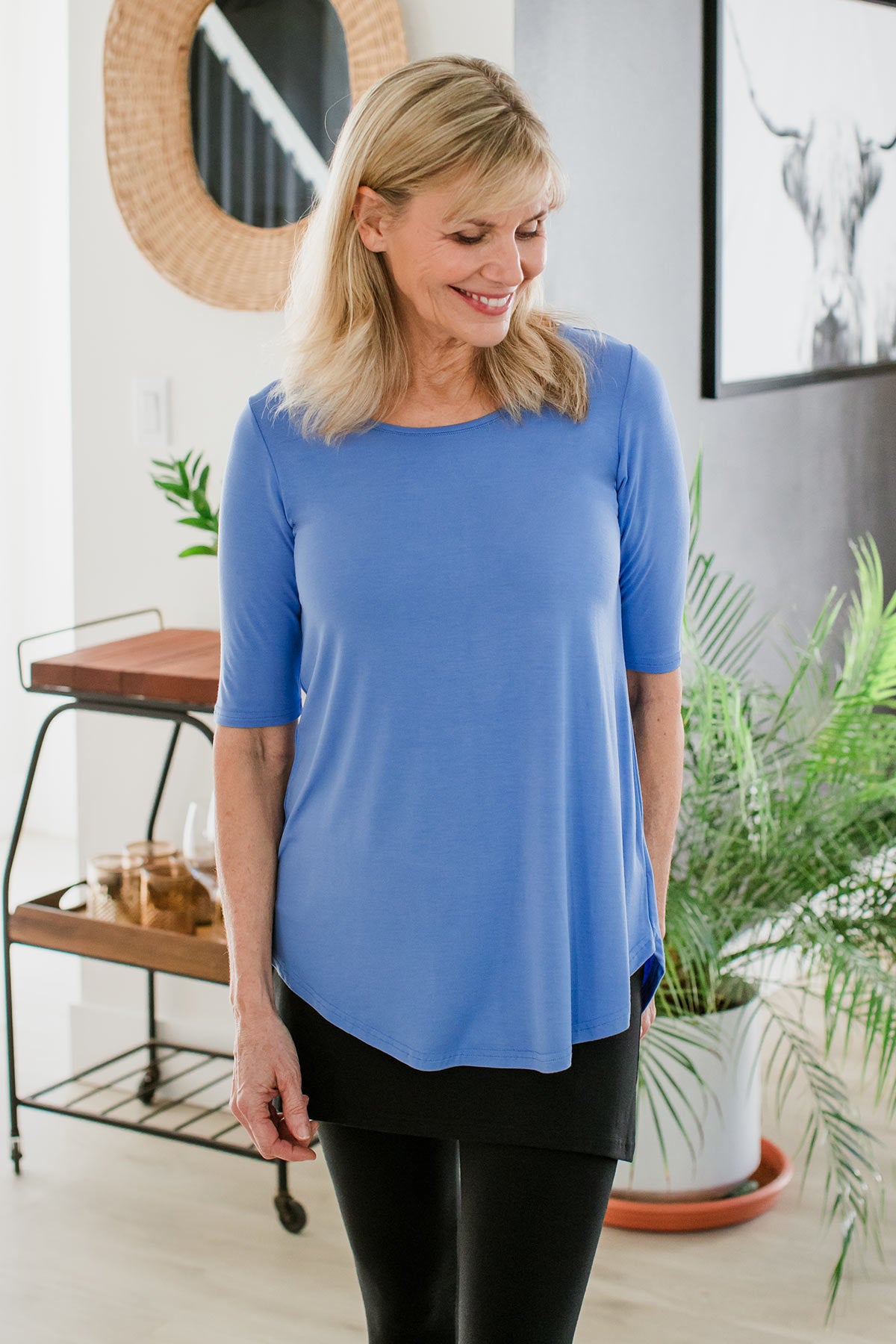 A woman with one hand in her pocket, looking down to the side and smiling, wearing Yala Sandy Relaxed Fit Scoop Neck Short Sleeve Bamboo Top in French Blue