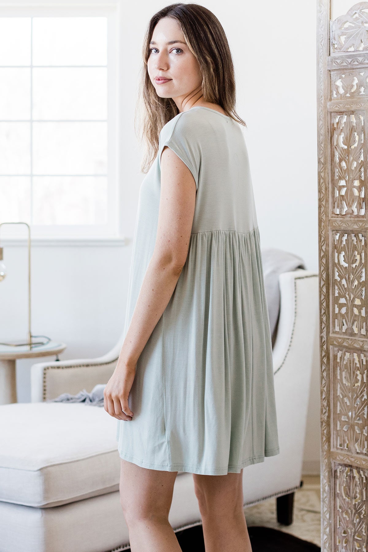 A woman facing away and looking back over her shoulder towards the camera, wearing Yala Opal Swing Bamboo Nightshirt in Honeydew