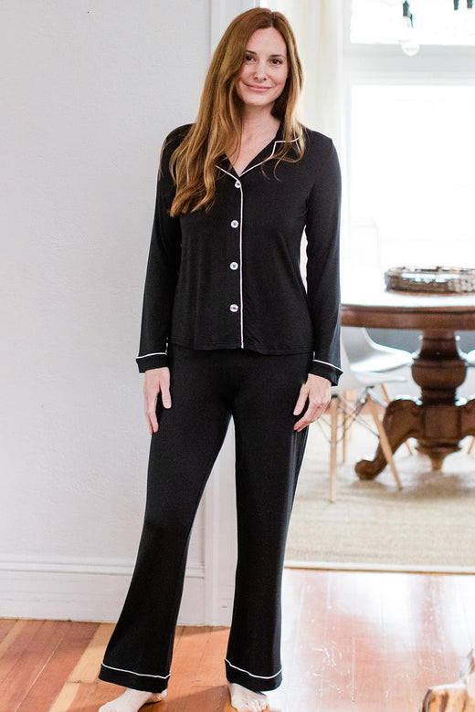 A woman standing ans miling with one leg stretched to the side, wearing Yala Amber Classic Button Front Bamboo Pajama Set in Black