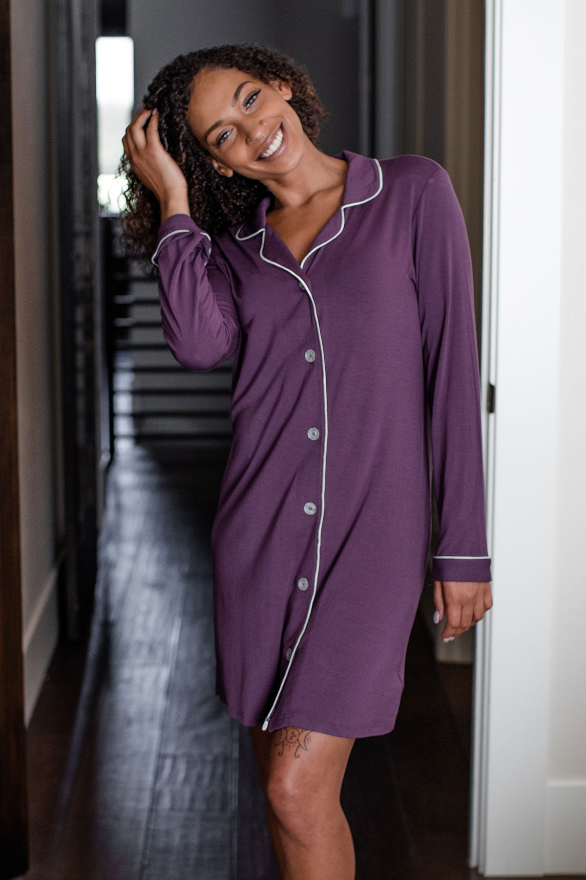 A woman standing and smiling with her head tilted to the side and her hand in her hair, wearing Yala Amber Classic Button Front Bamboo Nightshirt in Aster