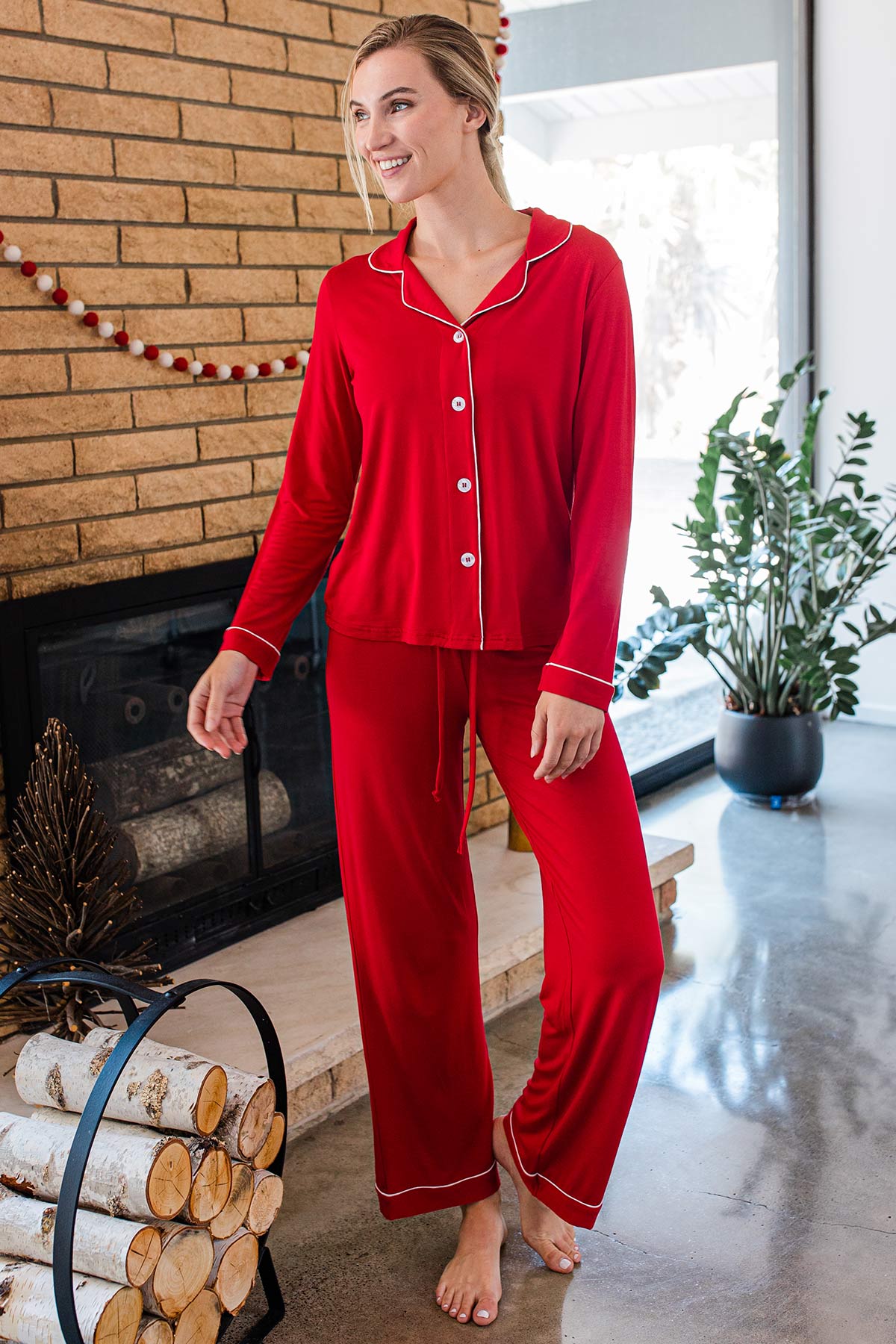 A woman standing and smiling with one knee bent, wearing Yala Amber Classic Button Front Bamboo Pajama Set in Crimson