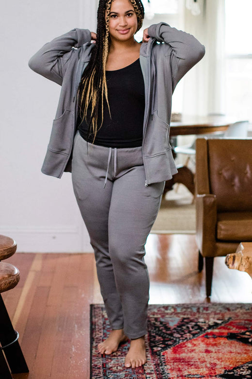 A woman standing with one foot forward while adjusting her jacket hood, wearing Yala Angel Bamboo and Organic Cotton Jogger Sweatshirt Lounge Pants in Space Grey