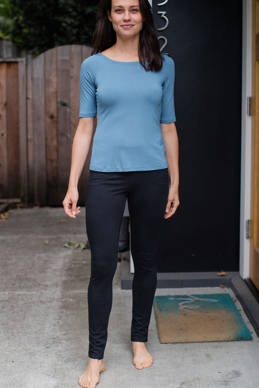 A woman standing and smiling with one foot forward, wearing Yala Beckett High-Waisted Bamboo and Organic Cotton Skinny Pants in Black