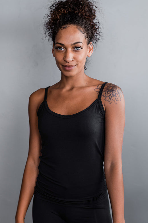 A woman standing and smilinng with both hands at her sides, wearing Yala Belle Cami Camisole Bamboo Tank Top in Black