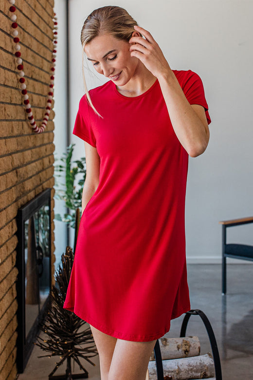 A woman standing with one hand in her pocket, looking downward and running a hand through her hair, wearing Yala Betsy Short Sleeve Fitted Bamboo Nightshirt in Crimson