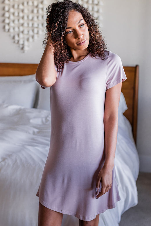 A woman standing and looking off to the side with one hand in her hair, wearing Yala Betsy Short Sleeve Fitted Bamboo Nightshirt in Lotus Pink
