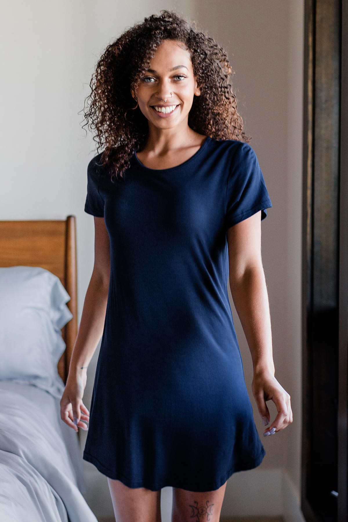 A woman standing and smiling with both hands at her sides, wearing Yala Betsy Short Sleeve Fitted Bamboo Nightshirt in Navy