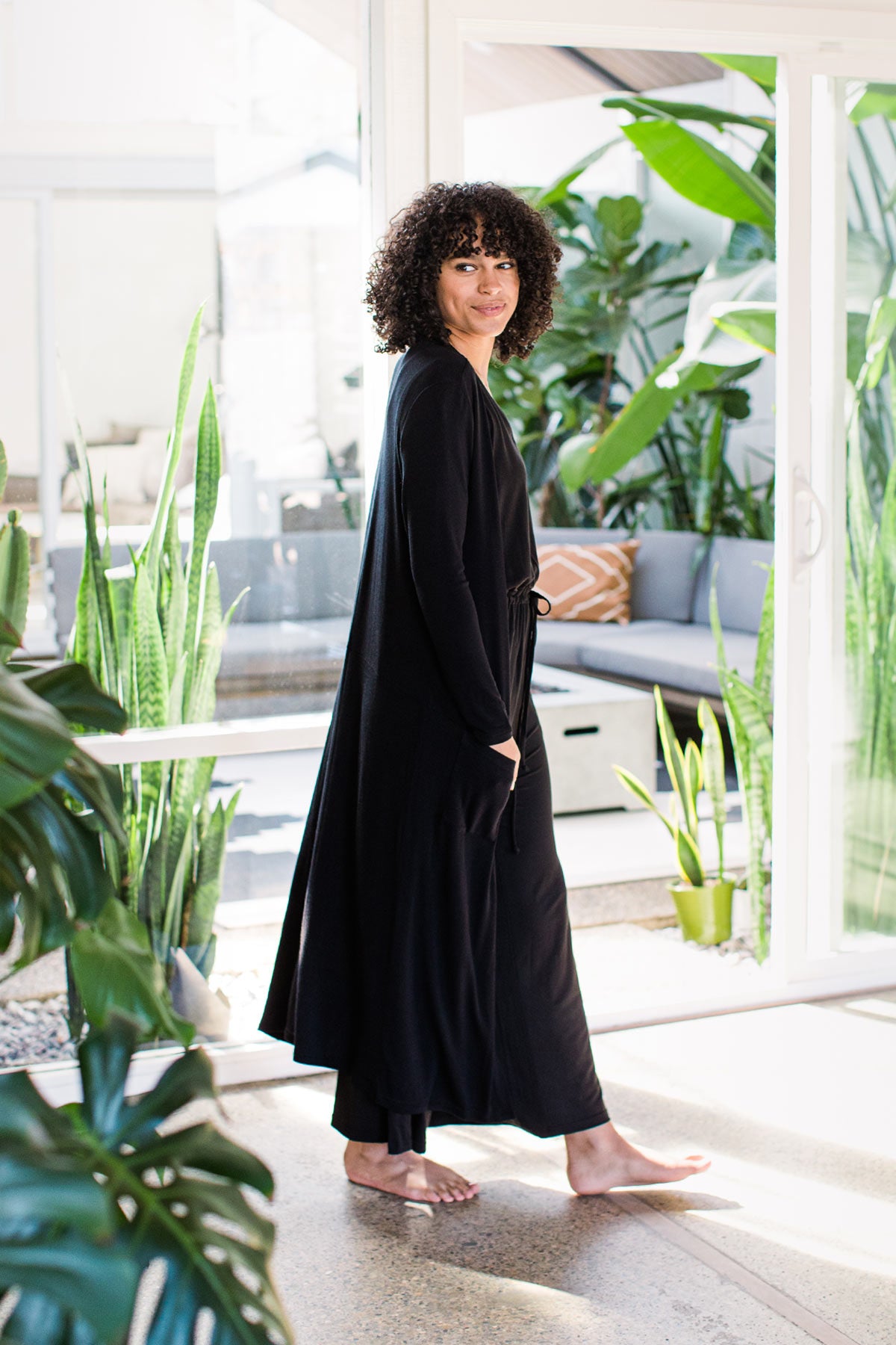 A woman walking and looking sideways at the camera, wearing Yala Brooke Cardigan Duster Bamboo Sweater in Black