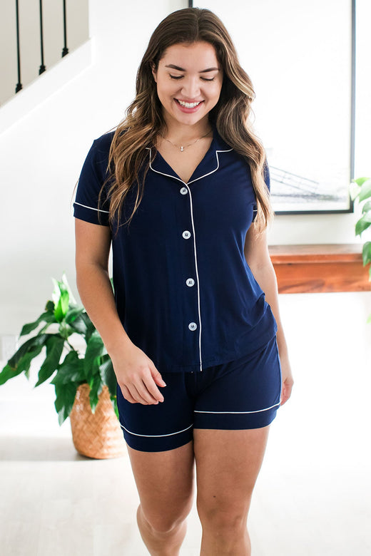 A woman walking towards the camera and looking downward with a smile on her face, wearing Emma Classic Button Front Shorts Bamboo Pajama Set in Navy