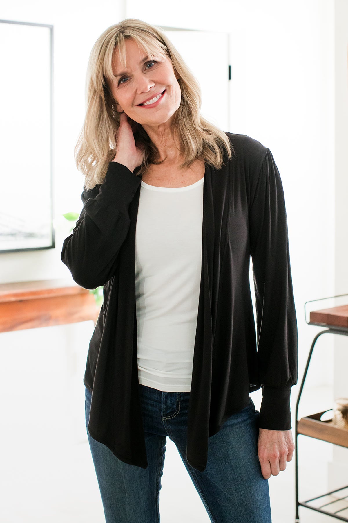 A woman standing with her head tilted, one hand at her side and one hand raise to the side of her neck, wearing Yala Everly Puffed Sleeve Bamboo Wrap in Black