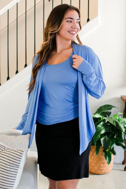 A woman standing and smiling while looking off to the side, wearing Yala Everly Puffed Sleeve Bamboo Wrap in French Blue
