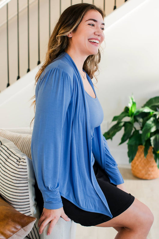 A woman sitting on the arm of a couch and smiling, wearing Yala Everly Puffed Sleeve Bamboo Wrap in French Blue