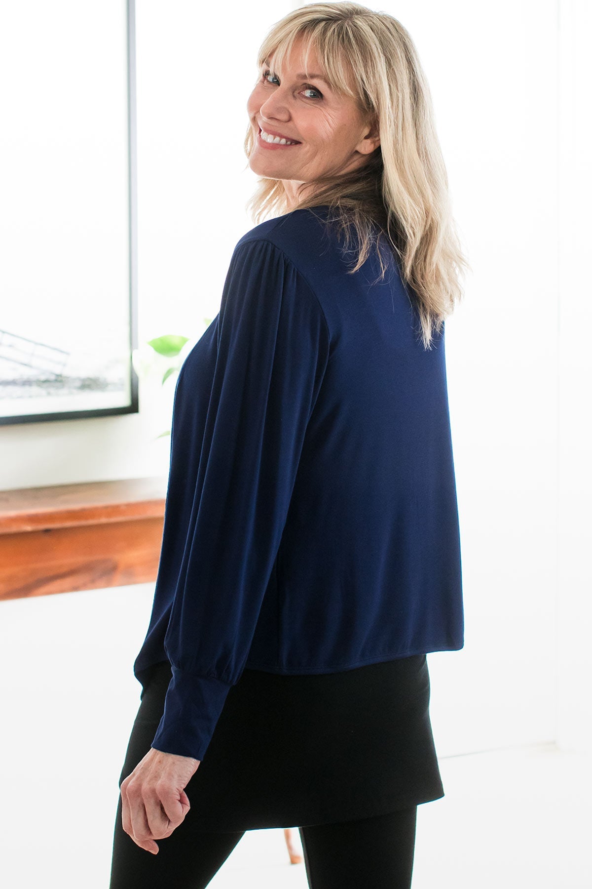 A woman standing with her back to the camera, looking over her shoulder and smiling, wearing Yala Everly Puffed Sleeve Bamboo Wrap in Navy