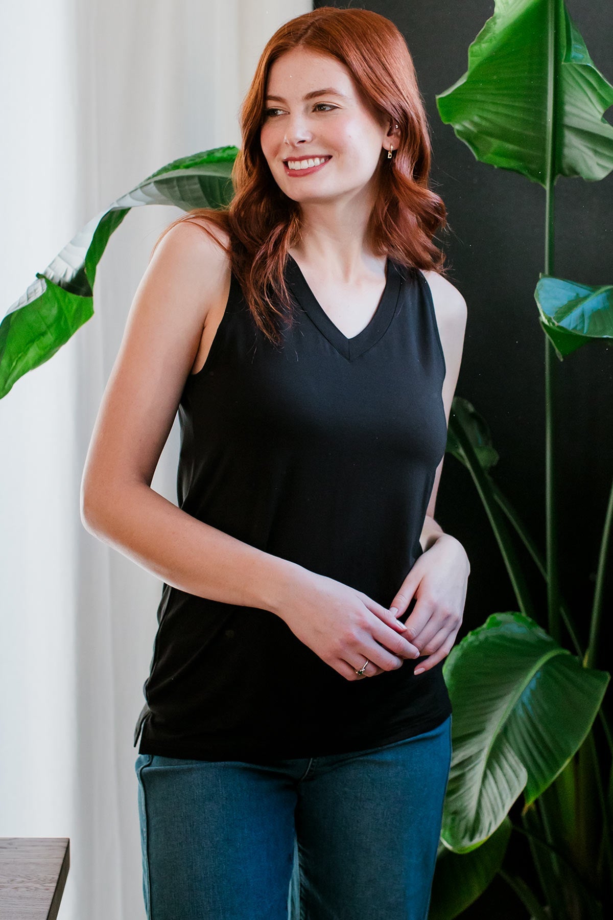 A woman standing with both hands held in front of her waist, wearing Ginger V-Neck Racerback Bamboo Tank Top in Black