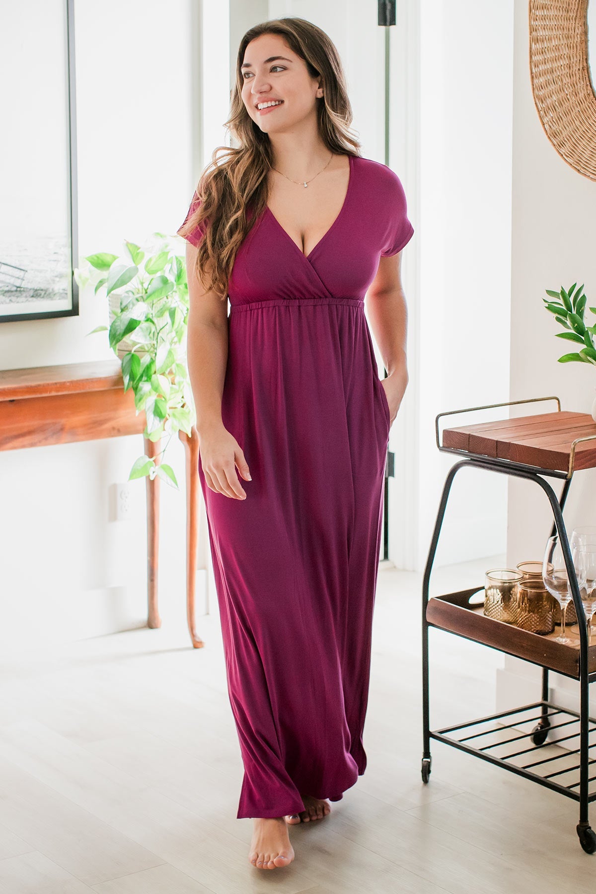 A woman standing with one hand in her pocket and looking off to the side with a smile on her face, wearing Zoey Crossover Bamboo Maxi Dress in Boysenberry