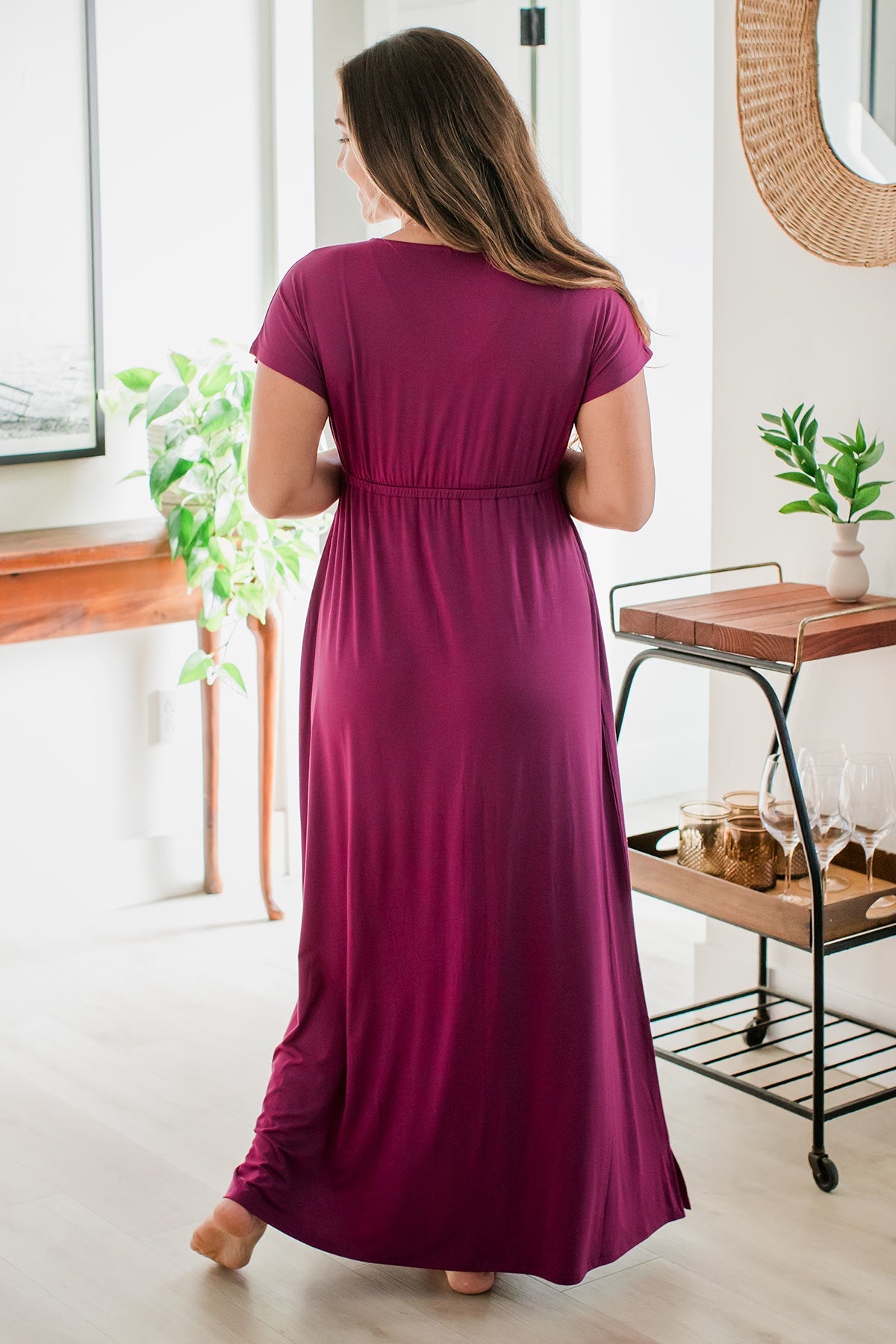 A woman standing with her back to the camera, one foot tilted up on its ball, wearing Zoey Crossover Bamboo Maxi Dress in Boysenberry
