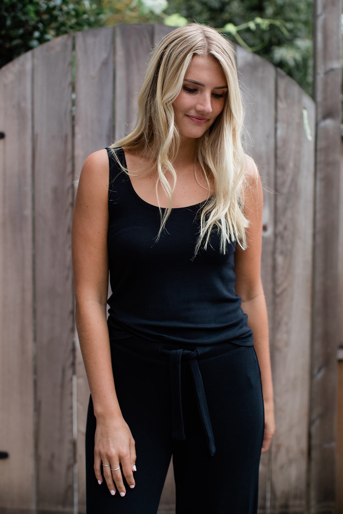 A woman standing with one arm forward and one arm back while looking down, wearing Yala Claire Bamboo Sweater Tank Top in Black