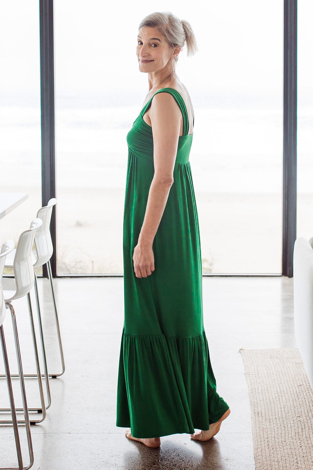 Woman facing away, turned and looking at the camera, wearing Yala Cleo Babydoll Bamboo Maxi Dress in Emerald