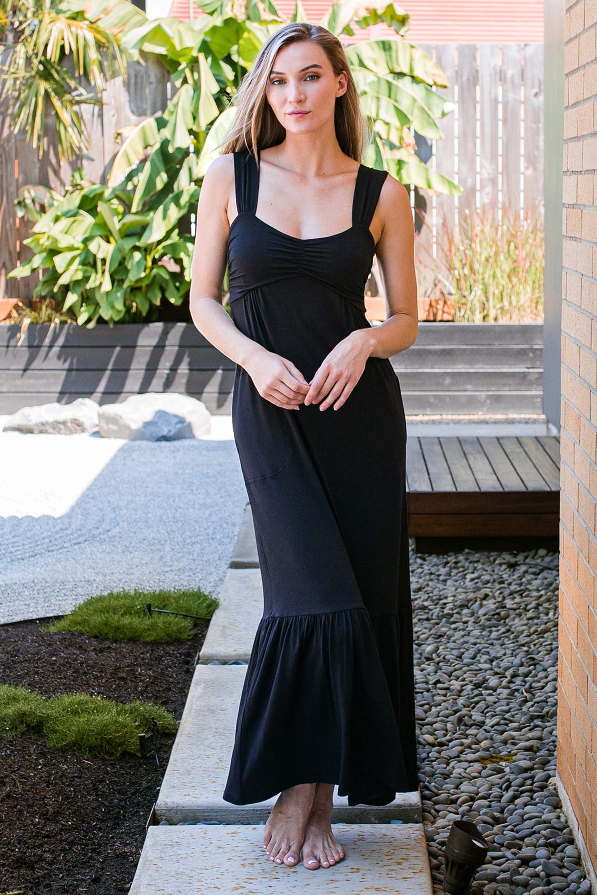 A woman standing with her hands together in front of her, wearing Yala Cleo Babydoll Bamboo Maxi Dress in Black