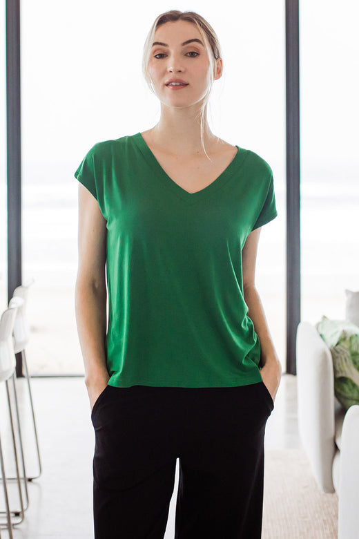 Woman standing with her hands in her pockets, wearing Yala Dakota V-Neck Cap Sleeve Bamboo Top in Emerald