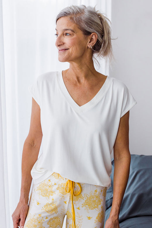 Womand standing and looking to the side while smiling, wearing Yala Dakota V-Neck Cap Sleeve Bamboo Top in Natural