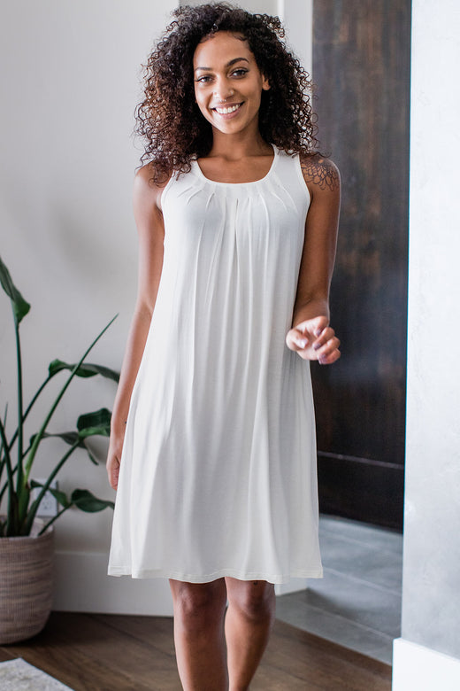 A woman standing and smiling with one hand reaching forward, wearing Yala Delia Gathered Tank Bamboo Nightgown in Natural