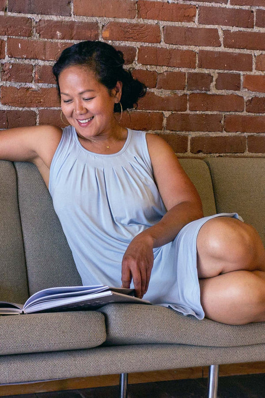 A woman sitting on a couch with her legs up while reading a book, wearing Yala Delia Gathere Tank Bamboo Nightgown in Sky