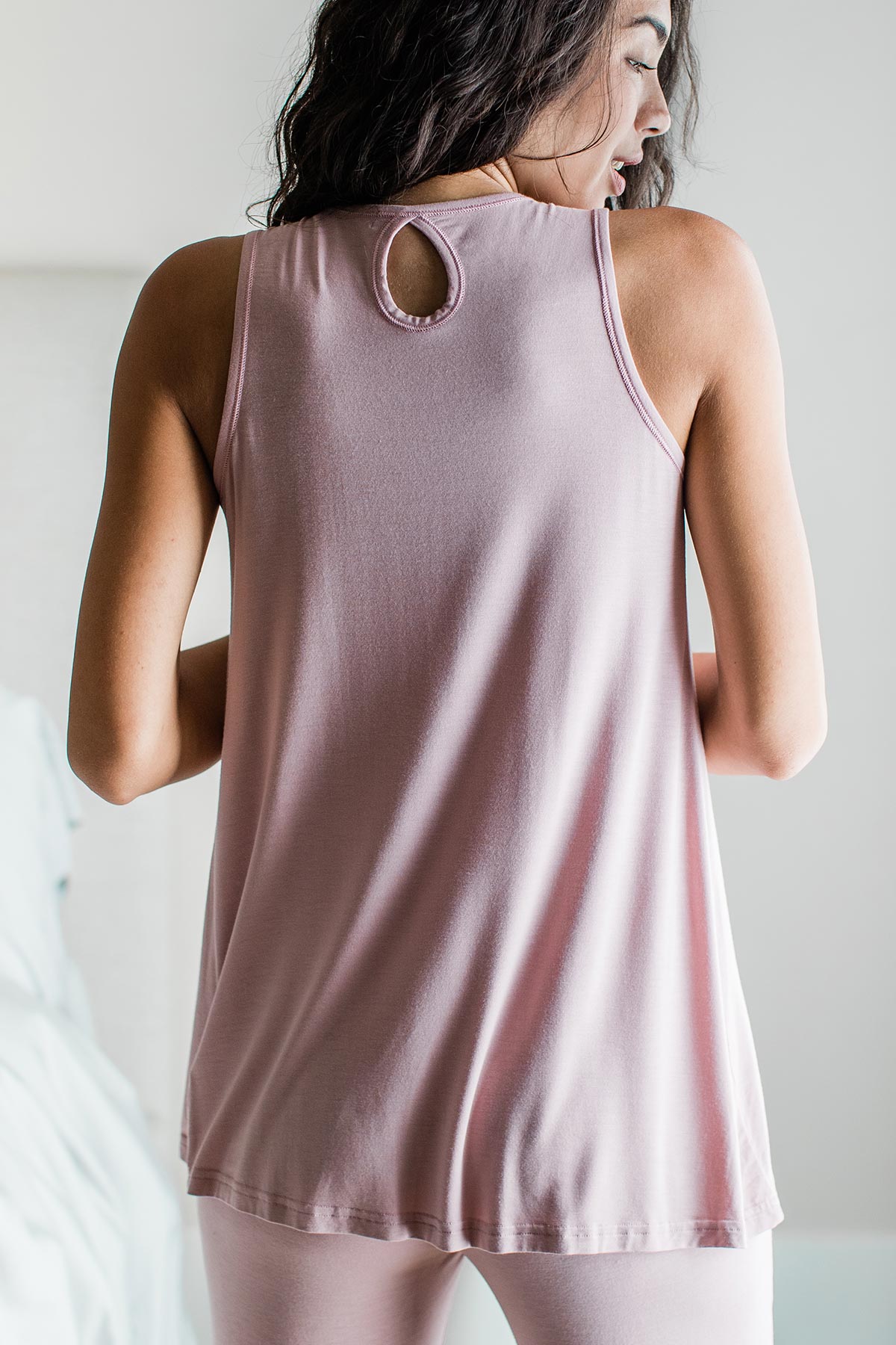 A woman standing with her back turned while looking off to the side, wearing Yala Delia Gathered Tank Bamboo Pajama Set in Lotus Pink