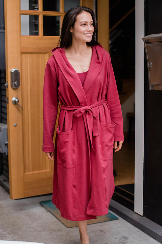 A woman walking out of a doorway and smiling, wearing Yala Elliot Bamboo and Organic Cotton Sweatshirt Hooded Robe in Rosewood