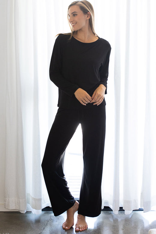 A woman standing and looking to the side, wearing Yala Gillian Piped Bamboo Pajama Pants in Black