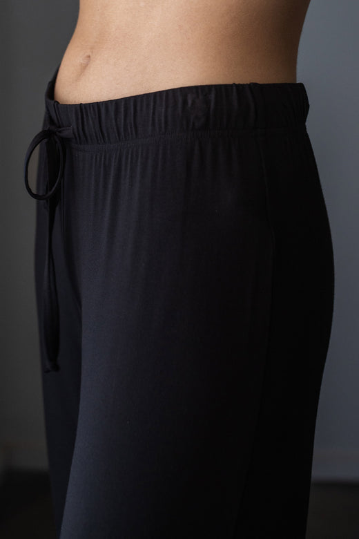 Close shot of a woman's waist and hips, wearing Yala Gillian Piped Bamboo Pajama Pants in Black