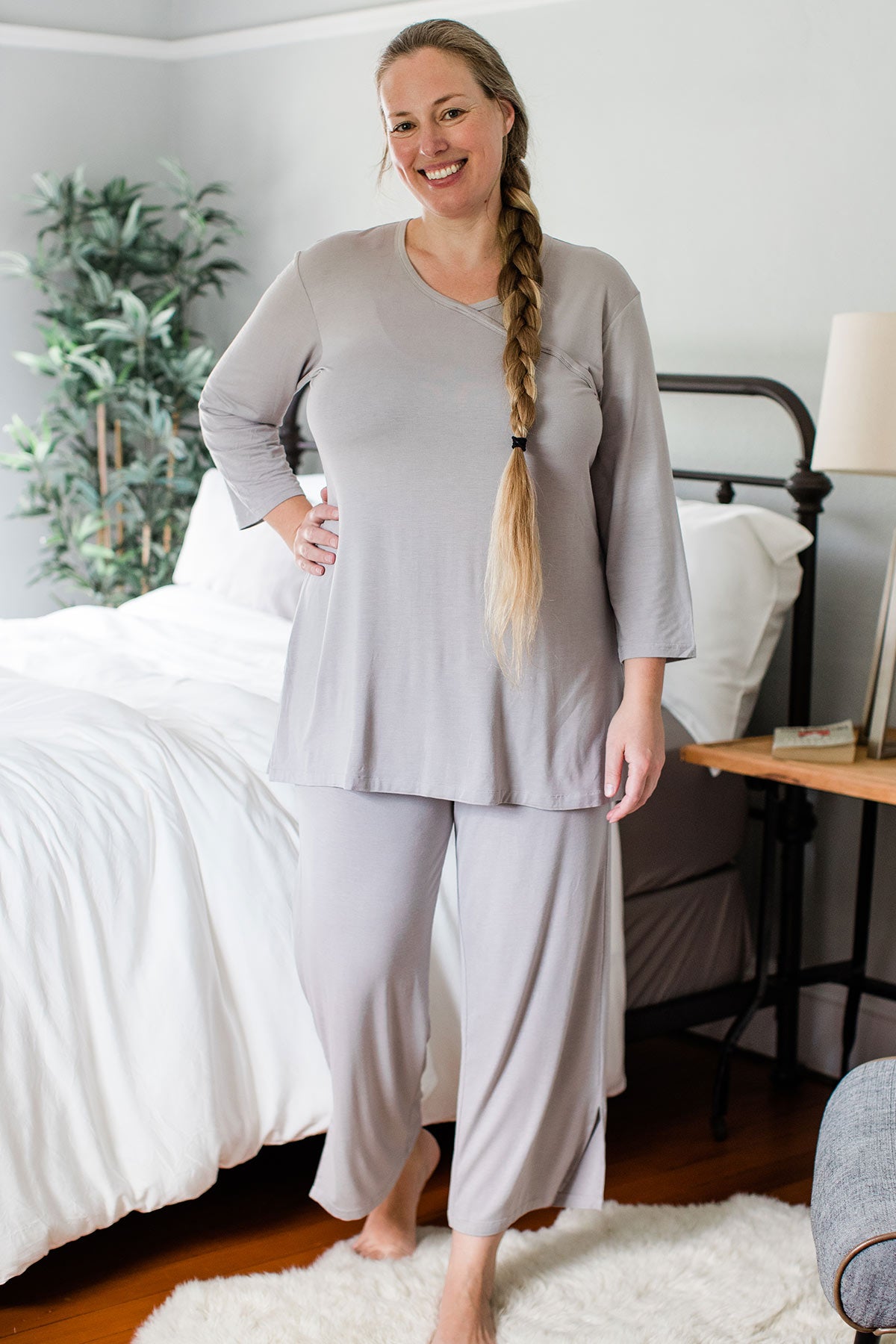 A woman standing and smiling with one hand on her hip, wearing Yala Haley Crossover Front Three Quarter Sleeve Bamboo Pajama Set in Ash