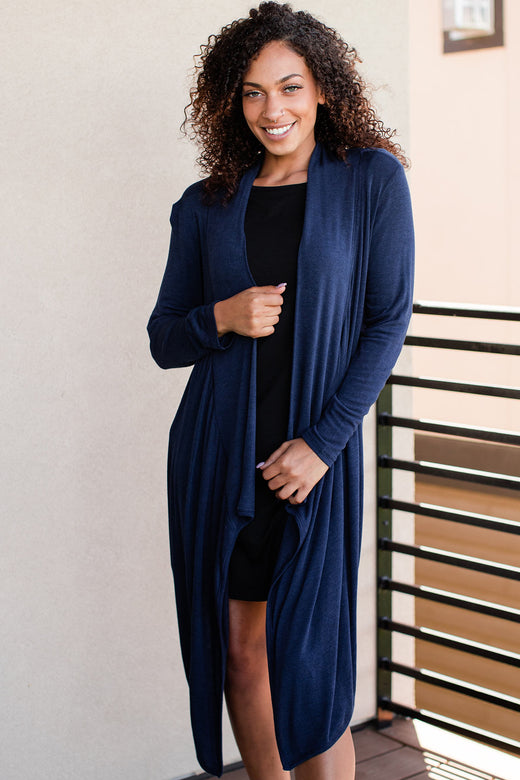 A woman standing and smiling with her hands holding the edges of her sweater, wearing Yala Hilary Bamboo Sweater Wrap in Navy