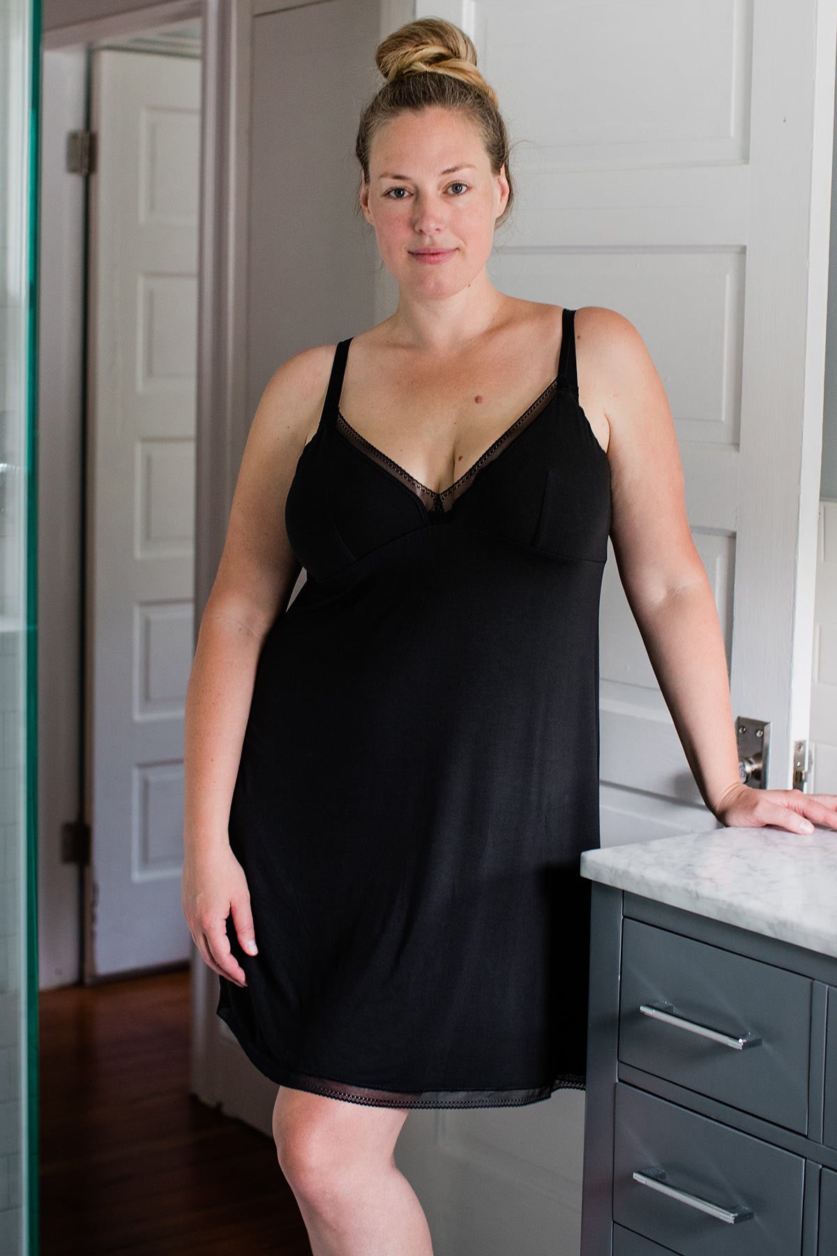A woman standing with one hand leaning against a countertop, wearing Yala Iris Lace Bamboo Nightgown in Black