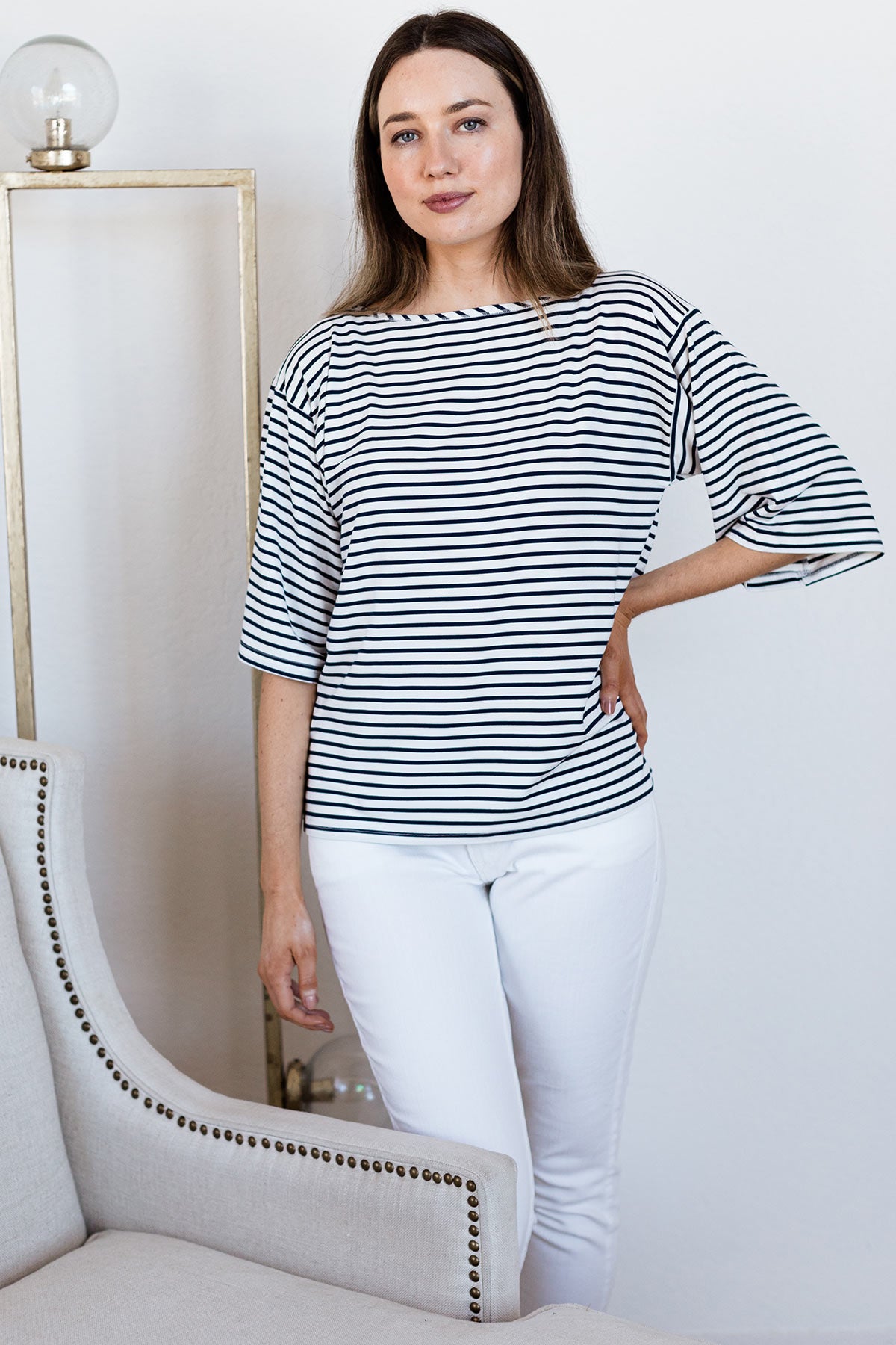A woman standing with one hand on her hip, wearing Yala Jaclyn Wide Sleeve Boatneck Bamboo Top in Navy Newport Stripe