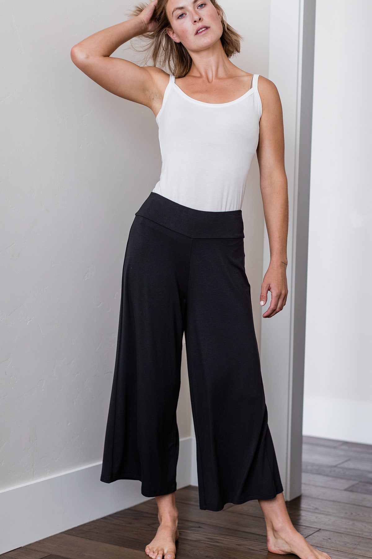 A woman standing with one leg outstretched and one hand in her hair, wearing Yala Jaden Wide Leg Cropped Bamboo Pants in Black